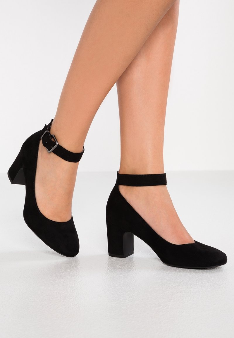 Talons en daim noir avec un bout rond, un talon bloc de hauteur intermédiaire et une sangle de cheville avec un détail de boucle en métal. Texture lisse, design élégant.