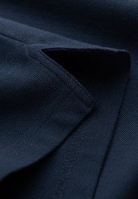 Námořnicky modrý látkový povrch s texturou, s ohnutým okrajem, který odhaluje čisté šití podél švu.