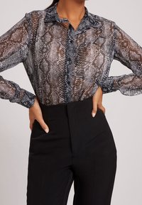 Blouse longue à manches longues en tissu transparent avec un motif imprimé serpent noir et marron, dotée d'un col, d'une fermeture boutonnée sur le devant et d'une coupe légèrement ample.
