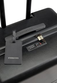 Black hardshell suitcase with a retractable handle, zipper closure, built-in combination lock, and a leather luggage tag labeled "ETERNITIV."