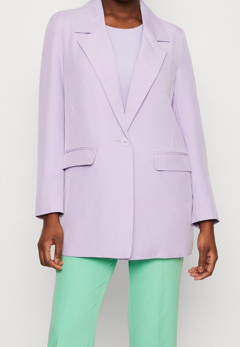 Blazer lilas avec un col cranté, une fermeture à un bouton et deux poches avant, assorti à un pantalon vert menthe. Tissu à texture lisse.