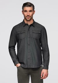 Chemise en denim gris foncé avec fermeture boutonnée, deux poches poitrine et col pointu. Manches longues avec poignets boutonnés et ourlet droit.