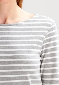 Maglietta a maniche lunghe grigio e bianco a righe con scollatura ampia e texture morbida, caratterizzata da righe orizzontali di larghezza variabile.