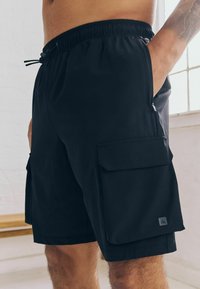 Sorte cargo shorts med elastisk talje, snor, sidelommer og lårlommer på hver side. Fremstillet af let, åndbart stof.