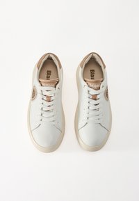 Sneaker bianchi in pelle con dettagli in tan, lati testurizzati e lacci piatti. Presentano un'etichetta con logo e una suola in gomma di colore chiaro.