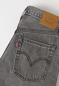 Πίσω τσέπη γκρι τζιν Levi's με καφέ δερμάτινη ετικέτα Levi Strauss & Co. και μικρή κόκκινη ετικέτα Levi's στη ραφή της τσέπης.
