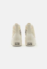 Wysokie trampki z płótna w kolorze kremowym z haftem w kwiaty, gumowymi podeszwami oraz szczegółem logo Converse na pięcie. Zamek z tyłu.