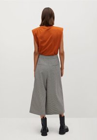 Haut court orange rouille à manches courtes avec épaulettes, associé à des culottes à carreaux gris et des bottines noires, vu de dos.