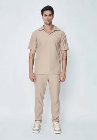 Polo shirt beige à manches courtes et pantalon tapered assorti, fabriqué à partir d'un tissu doux. La tenue présente un col pointu et un design minimaliste.