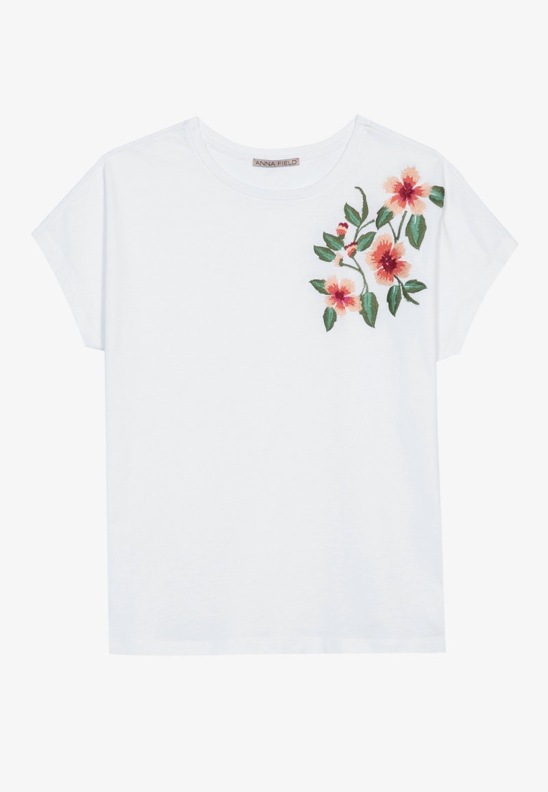 T-shirt blanc à manches courtes avec broderie florale rouge et rose et feuilles vertes sur le haut du torse à gauche.