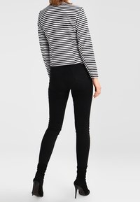 Randig långärmad topp med en kortad design, kombinerad med svarta slim-fit jeans och högklackade skor. Outfiten har ett modernt, åtsittande utseende.