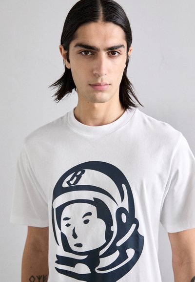 White cotton t-shirt featuring a large black astronaut graphic on the front. The design includes a prominent helmet and facial outline.