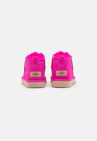 Stivaletti alla caviglia in suede rosa brillante con fodera in pelliccia morbida, dotati di un'etichetta con logo e suola in gomma testurizzata.