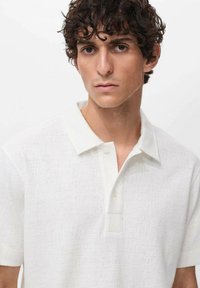 Hvid tekstureret polo t-shirt med korte ærmer, en spredt krave og knaplukning. Stoffet har et subtilt vævemønster.
