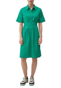 Zielona sukienka koszulowa z krótkim rękawem wykonana z bawełny, z zapinanym przodem, dopasowaną talią i długością do kolan, w połączeniu z trampkami.