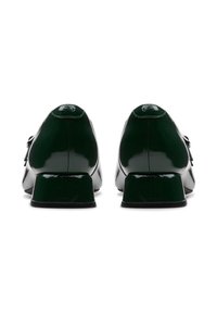 Une paire de chaussures en cuir verni vert foncé avec des talons carrés, vue de l'arrière sur fond blanc.