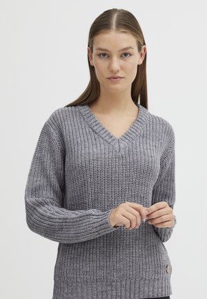 Pull en tricot gris à col en V, avec des poignets et un ourlet à côtes. Présente un motif texturé et un petit logo en accent sur le côté.