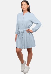 Abito camicia azzurro chiaro in tessuto texture, con cintura da annodare in vita e maniche lunghe. Abbinato a sneakers bianche.