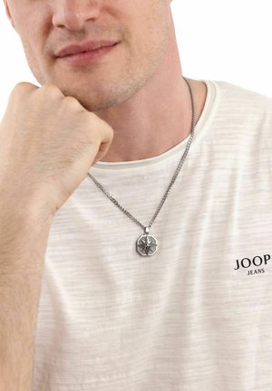 Hombre con una camiseta blanca de JOOP Jeans y un collar de cadena plateada con un colgante en forma de estrella octogonal.