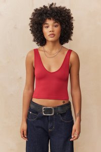 Top in cotone rosso a costine con scollo a V profondo, abbinato a jeans in denim scuro a vita alta e una cintura nera con fibbia metallica.