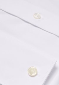 Camicia bianca in morbido cotone, con due bottoni rotondi di un beige chiaro e un patto cucito. Leggera lucentezza e texture.
