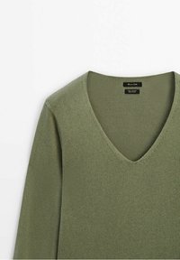 Pull en tricot vert olive avec col en V et manches longues, étalé à plat sur un fond blanc.