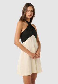 Halter-neck kjole med en svart topp og en kremfarget skjørt, med en tettsittende liv og flytende silhuett. Glatt stoff og minimalistisk design.