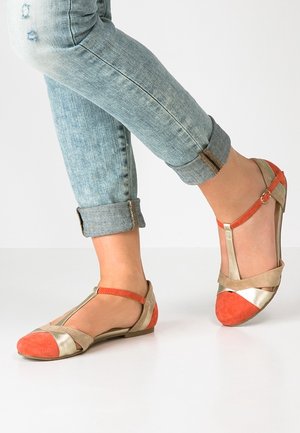 Flade sko med et farveskema i guldmetal, beige og orange. Funktioner inkluderer et T-rem-design og kontrasterende ruskindsaccents.