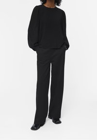 Blouse noire à manches longues avec un col rond et des manches bouffantes, associée à un pantalon noir ample. Les deux sont en tissu lisse.