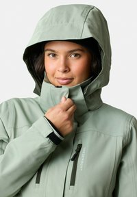 Soft green waterproof jacket with a hood, zippered chest pocket, adjustable cuffs, and sturdy material. Features a smooth, matte texture.