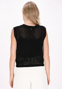 Top in maglia senza maniche di colore nero con un motivo testurizzato e a trama aperta. Presenta un collo rotondo e un orlo strutturato, abbinato a pantaloni bianchi.