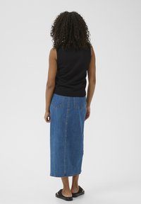 Haut sans manches noir, jupe maxi en denim, deux poches arrière, couleur bleue, texture lisse, et sandales noires plates au design minimal.