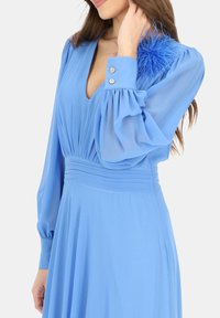 Jasnoniebieska sukienka z głębokim dekoltem, plisowanym korpusem, długimi, zwiewnymi rękawami oraz piórowym akcentem na lewym ramieniu.