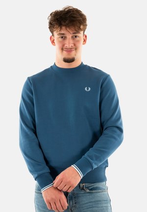 Felpa blu con collo rotondo, polsini a costine e logo decorativo bianco sul petto. Il materiale sembra morbido e ha una consistenza liscia.