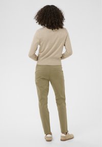 Pull en maille beige avec un col rond, associé à un pantalon vert olive et des baskets marron clair, présentant une texture lisse et une coupe ajustée.