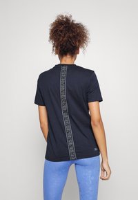 Svart kortärmad t-shirt med ett vertikalt vitt logostrand på baksidan, tillverkad av mjukt tyg med en avslappnad passform.