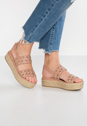 Sandalias de plataforma en rosa rubor con detalles de ojales dorados, suela intermedia de yute trenzado y correa ajustable en el tobillo. Combinadas con vaqueros de dobladillo deshilachado.