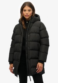 Chaqueta de plumón negra con capucha, que presenta un diseño acolchado, cremallera frontal y bolsillos laterales. Fabricada con un material suave e insulated.