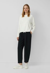 Witte top met lange mouwen en een zoom met trekkoord, gecombineerd met zwarte taps toelopende broek en witte sneakers, met een ontspannen pasvorm en eenvoudig design.