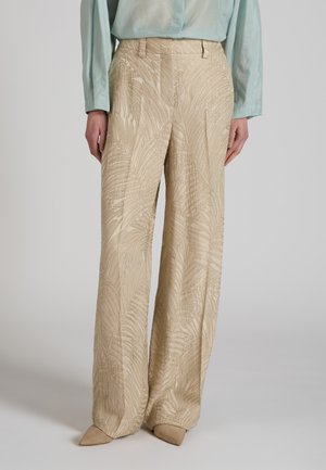 Pantaloni beige a gamba larga con motivo a foglie testurizzato indossati con una blusa a maniche lunghe azzurro chiaro e scarpe beige con punta appuntita.