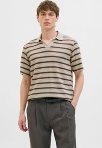 Polo cu mânecă scurtă, de tip v-neck, în dungi bej și maronii, având o textură netedă și guler cu petice, asortat cu pantaloni gri.