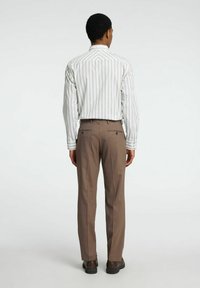 Witte en beige gestreepte shirt, lange mouwen, met knoopsluiting bij de manchetten, gecombineerd met een bruine broek. De broek heeft achterzakken met knoopsluitingen.
