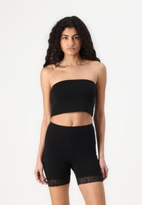 Svart crop top med en stroppeløs design sammen med høyhalsede shorts. Shortsene har blonder langs kanten. Myk, elastisk stoff.
