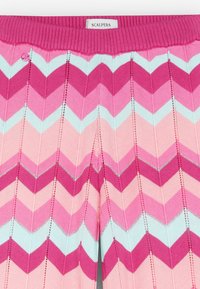 Vaaleanpunaiset ja siniset chevron-kuvioiset neulehousut, joissa on ribbineulevyötärö. Mukana pieni vaaleanpunainen nappiyksityiskohta vyötärön läheisyydessä.