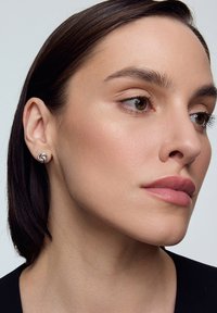 Srebrne kolczyki z ćwiekami o zakręconym wzorze, noszone na uchu modelki, podkreślone gładką skórą i neutralnym makijażem.