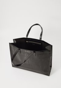 Bolsa tote preta brilhante com textura de crocodilo, duas alças e um bolso interior com fecho visível no interior.