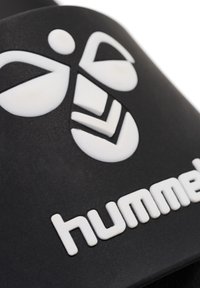Svart gummisandal med en vit bi-logotyp och "hummel" text. Slät matt yta med en minimalistisk stil.