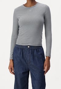 Långärmad randig topp i svart och vitt med rund halsringning, kombinerad med lösa blå denimbyxor med elastisk midja.