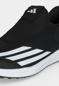 Μαύρο αθλητικό παπούτσι slip-on με λευκή σόλα και τρεις λευκές διαγώνιες ρίγες στο πλάι, με μικρό λογότυπο στη γλώσσα.
