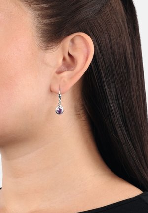 Srebrne kolczyki w kształcie obręczy z łezkowatym purpurowym kamieniem, wiszące na delikatnej pętli, o polerowanej powierzchni i lekko odbijającym światło wzorze.